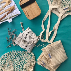 flat lay of resuable eco-friendly and zero-waste products including a string bag and steel pegs on a teal tablecloth