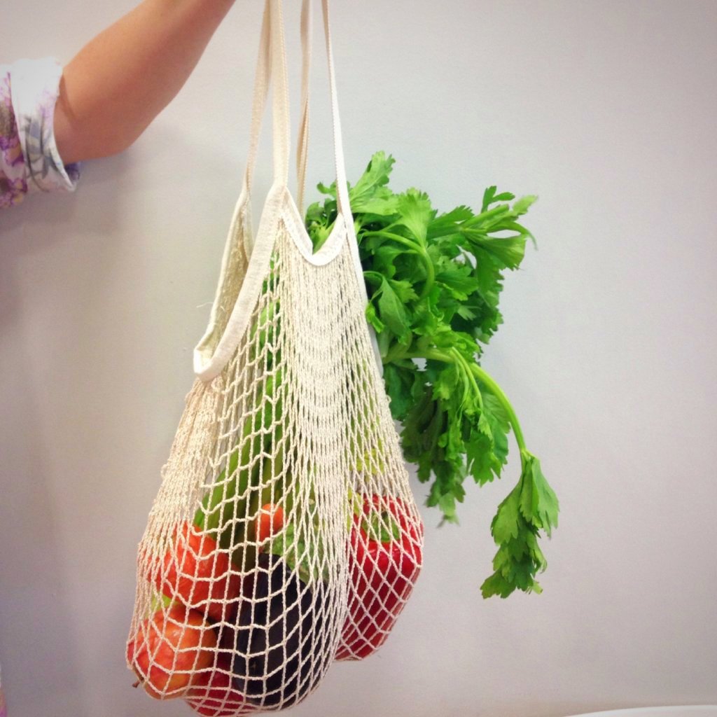 woman's arm holding a reusable string bag containing fresh vegetables